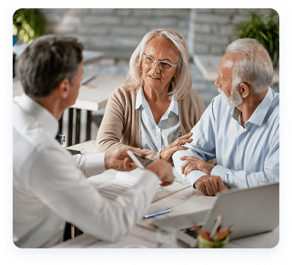 A financial advisor discusses paperwork with an attentive couple at a desk, in a well-lit office environment.