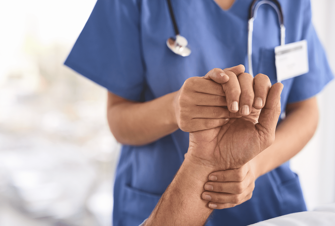 A healthcare professional in blue scrubs is checking the pulse on a patient's wrist.