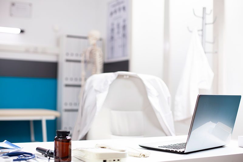 A modern office space is equipped with a laptop, documents, and medical supplies on the desk, under bright lighting.