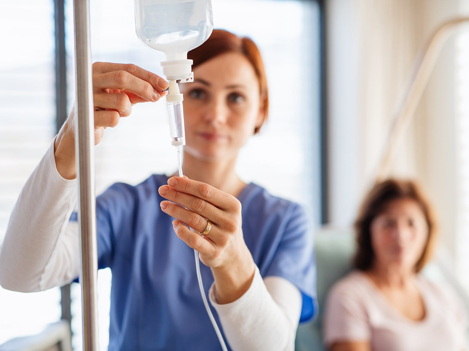 A healthcare worker adjusts an IV drip in a hospital room, focusing intently on her task.