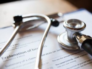 A stethoscope rests atop a medical document titled "Medical Examination" on a wooden table.