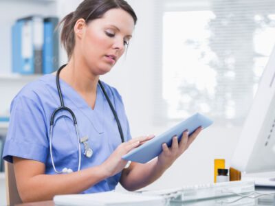 A healthcare professional in blue scrubs is focused on reviewing information on a tablet.