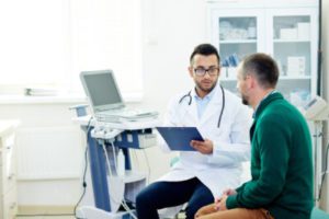 A medical professional is discussing health details with a patient in a clinic, with a laptop open nearby.