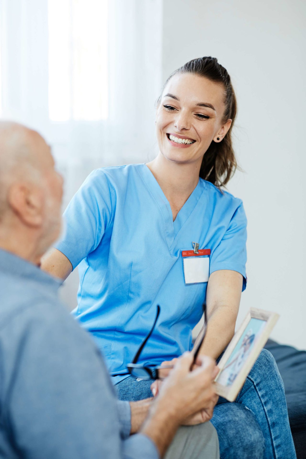A healthcare professional in blue scrubs is smiling while consulting with a patient, showing a document.