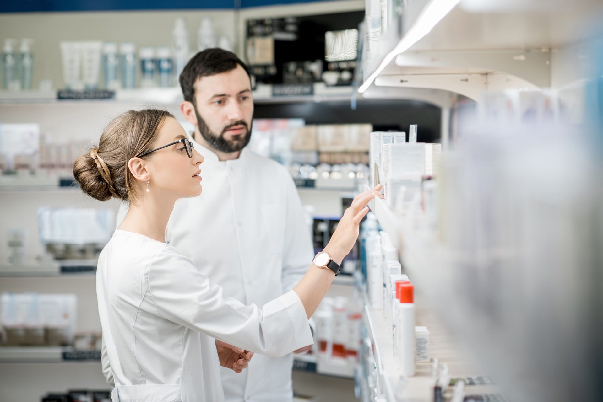 Two lab technicians in white coats are examining or discussing products on a shelf in a laboratory.