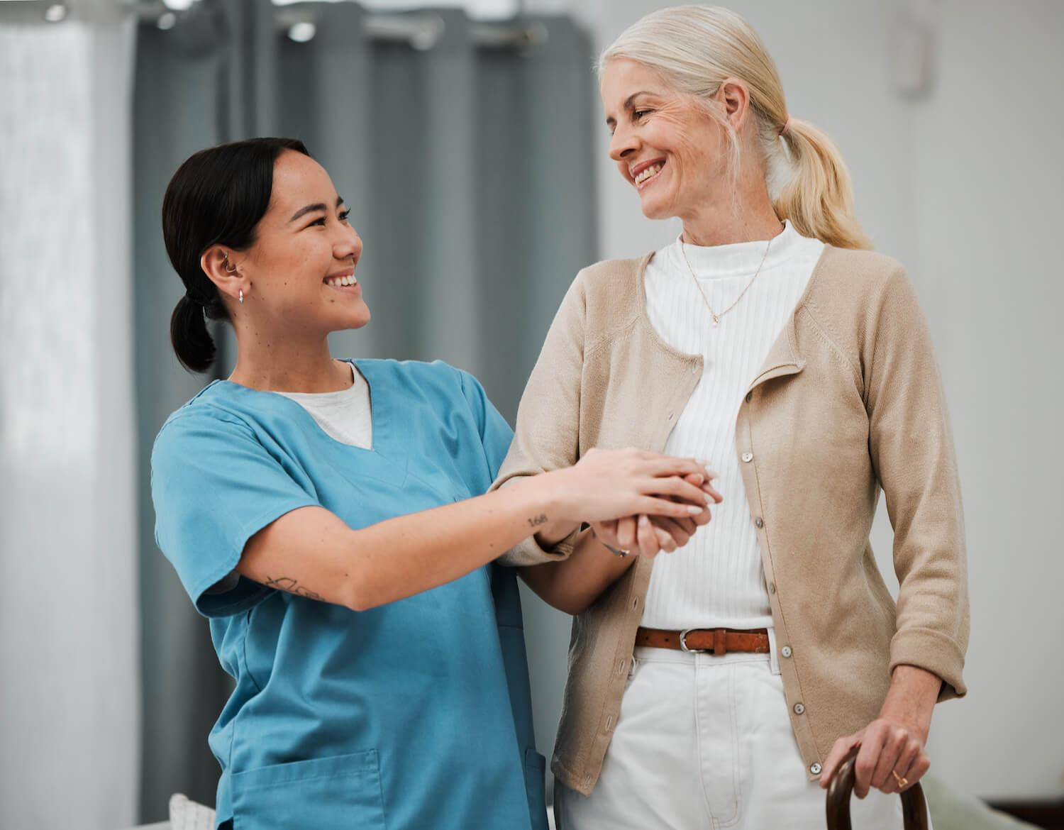 A healthcare worker assists an elderly woman with a friendly, supportive gesture in a clinical setting.