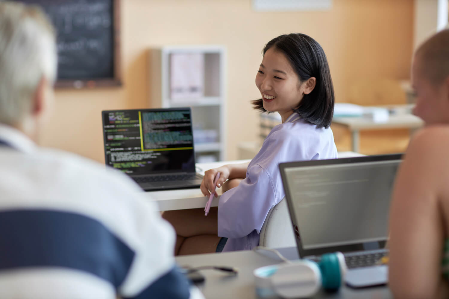 A smiling healthcare professional discusses information on a computer monitor with a colleague in a clinic office.